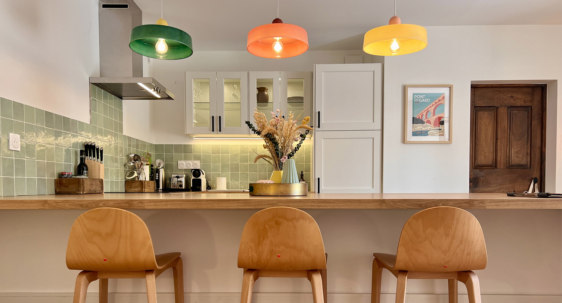 Cuisine équipée du gîte La Réserve à Sabran, avec bar et suspensions colorées.