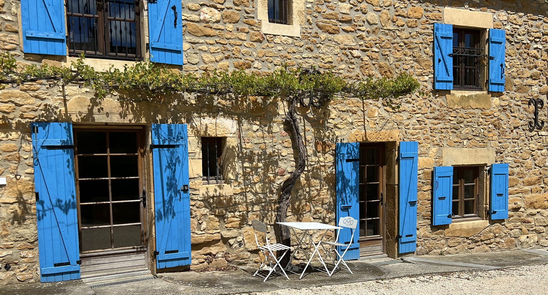 Façade en pierre du gîte La Réserve à Sabran, avec volets bleus, vigne