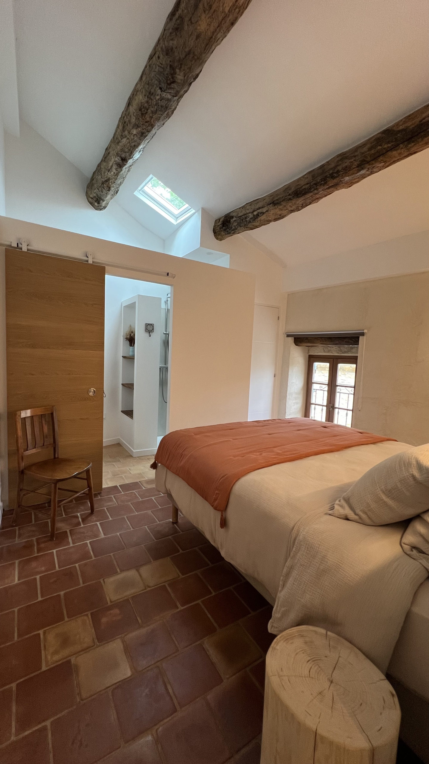 Chambre double du gîte La Grange avec poutres apparentes, fenêtre de toit et accès à la salle d’eau