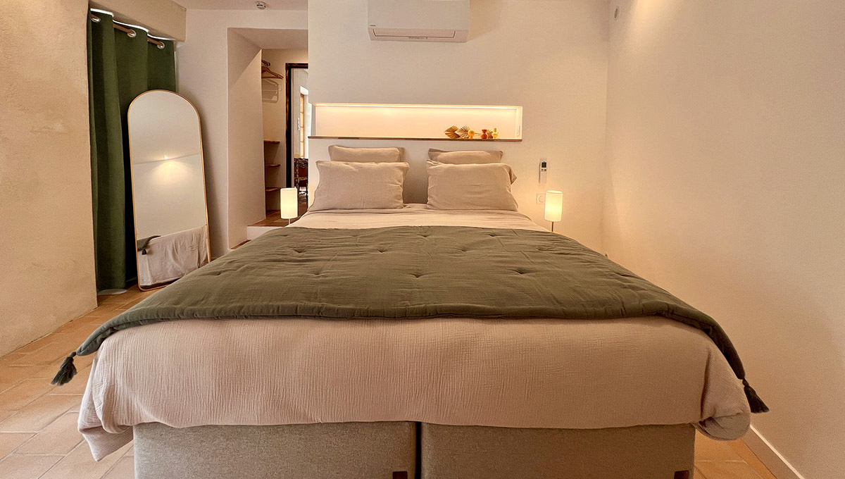 Chambre du gîte La Réserve à Sabran, avec lit double 160 × 200 cm, linge blanc, couvre-lit vert et éclairage en tête de lit