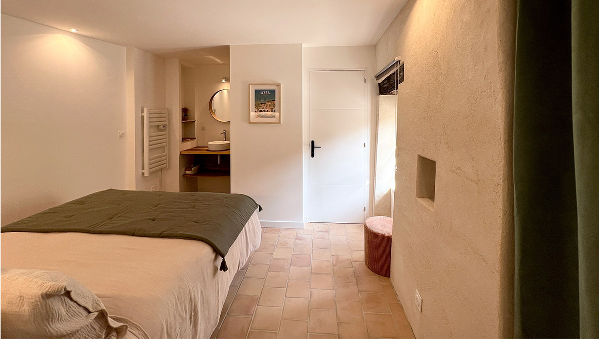 Chambre du gîte La Réserve à Sabran, avec lit double, sol en terre cuite et salle d’eau ouverte