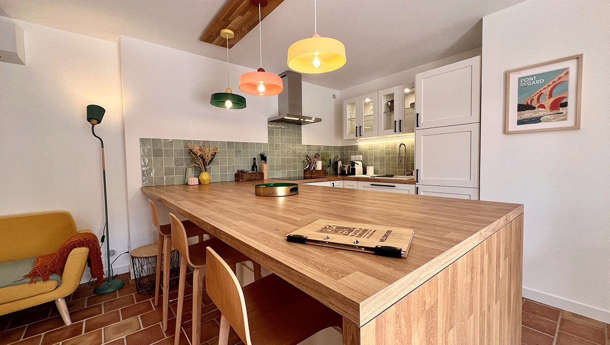 Cuisine équipée du gîte La Réserve à Sabran, avec grand bar en bois, tabourets et suspensions colorées